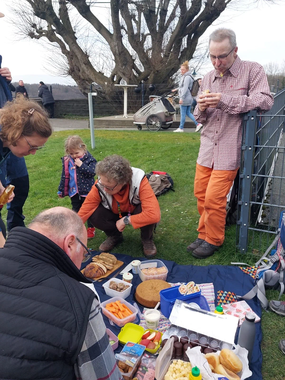 Picknickdecke mit Essen, Teilnehmer stehen und hocken darum