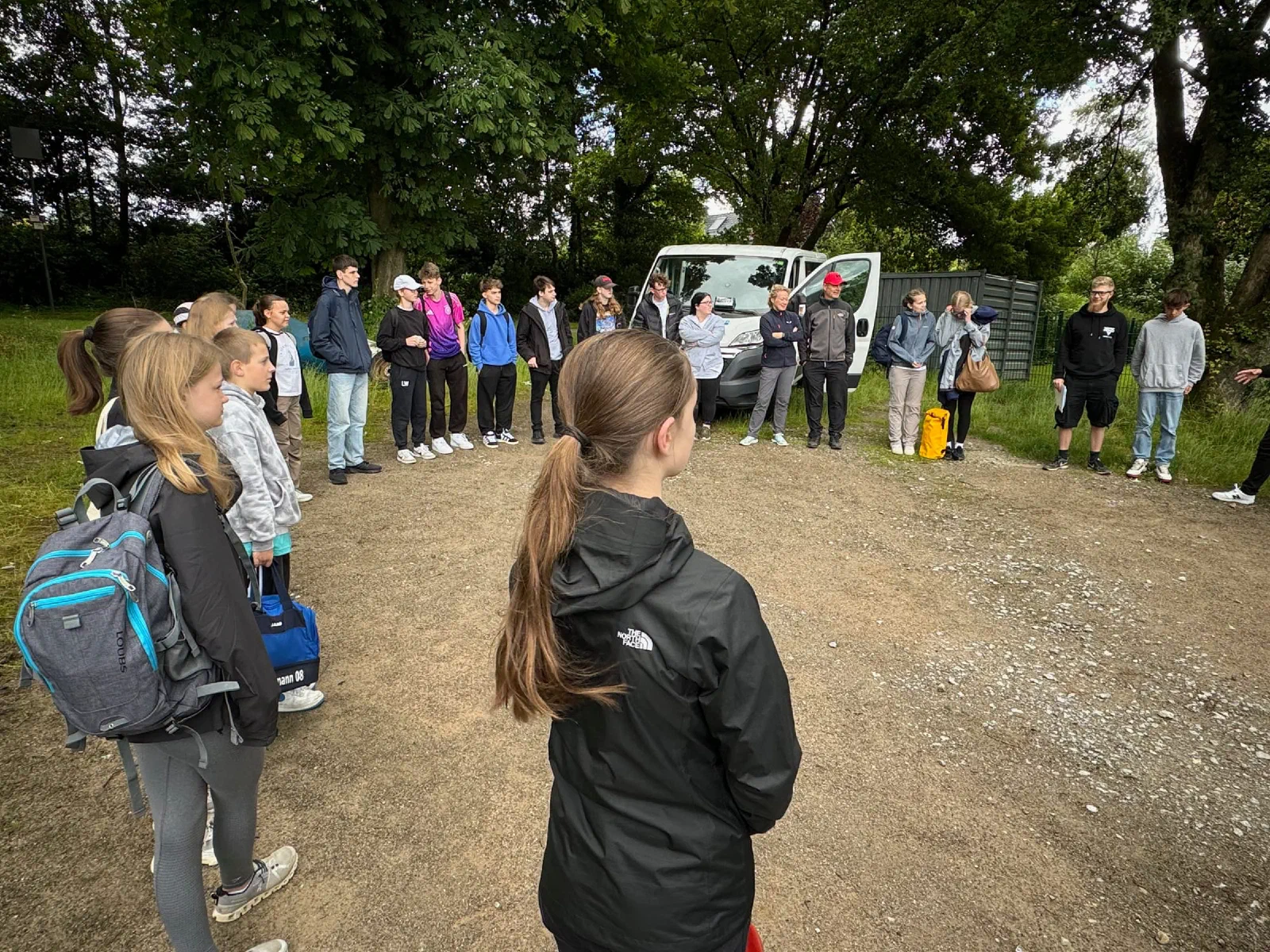 Die Gruppe steht im Kreis auf der Wiese und hört die Einweisung