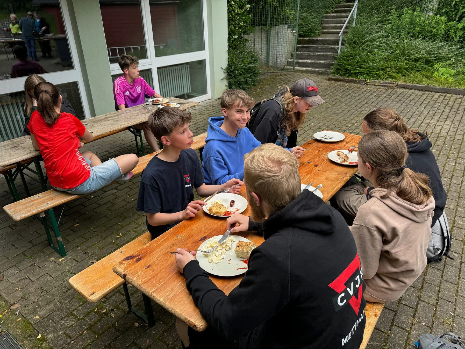 Jugendliche essen an Bierbänken, einer trägt einen CVJM-Pullover